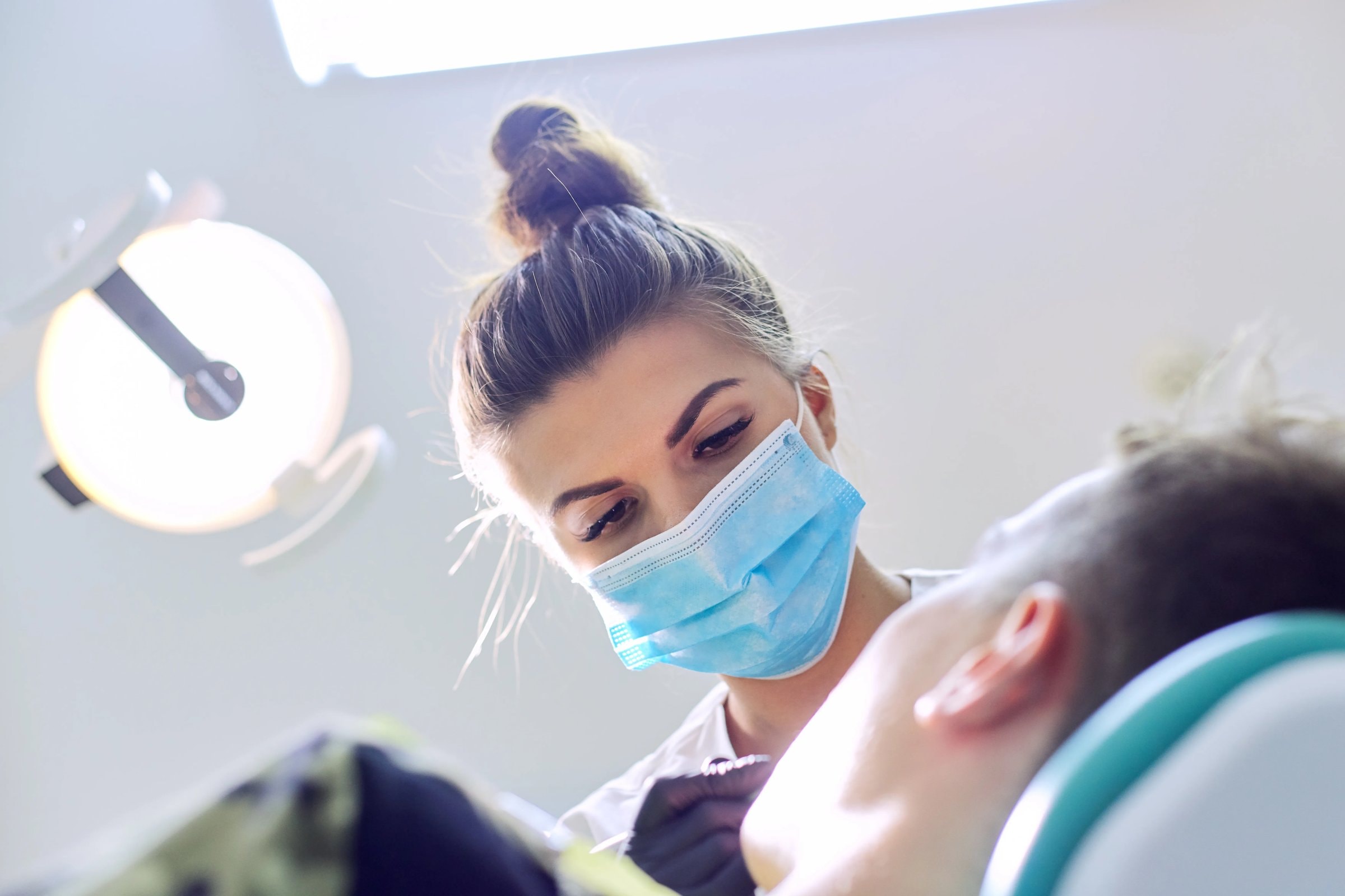A hygienist in a mask carefully cleaning a patient's teeth