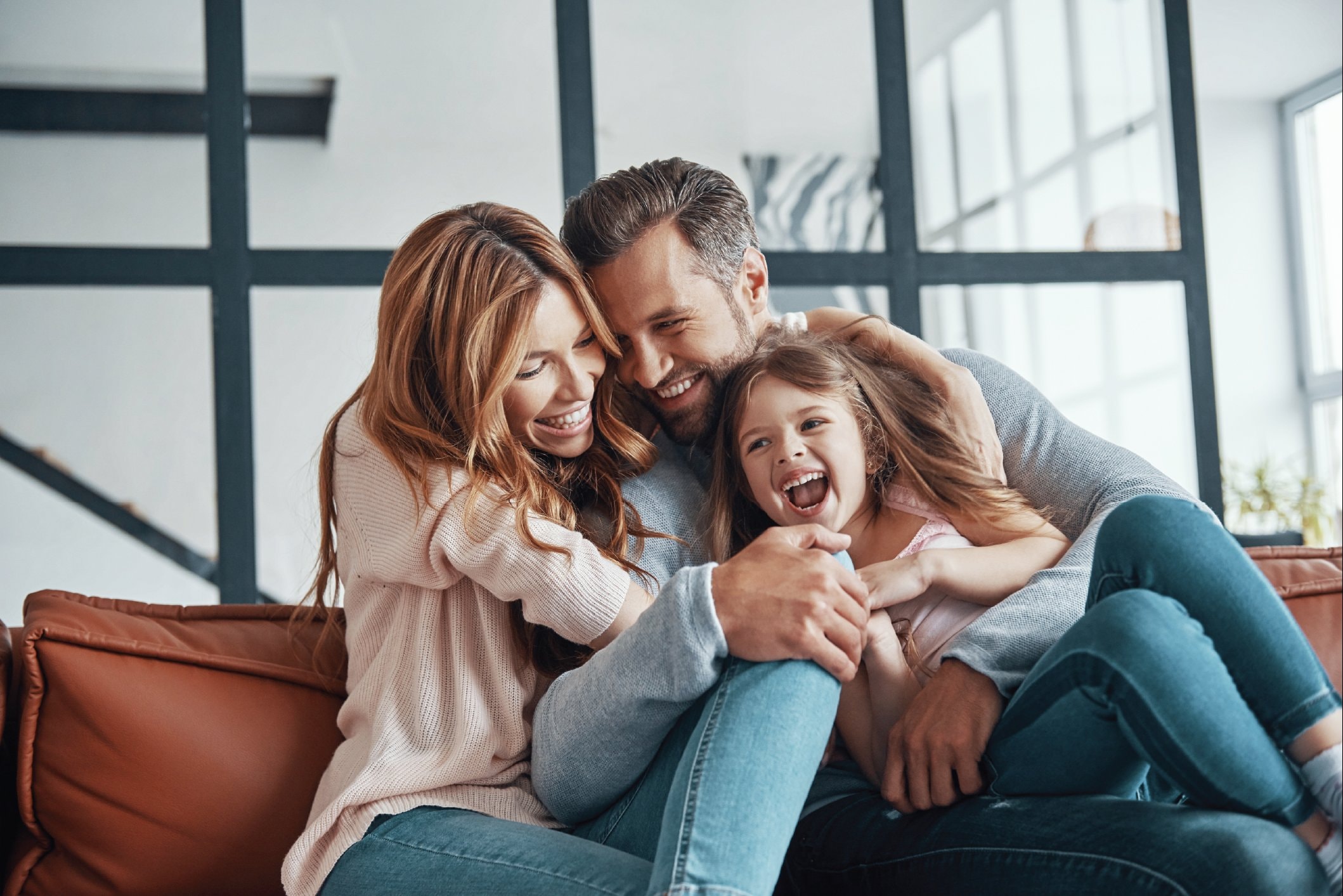 Parents and their young daughter laughing together on the sofa