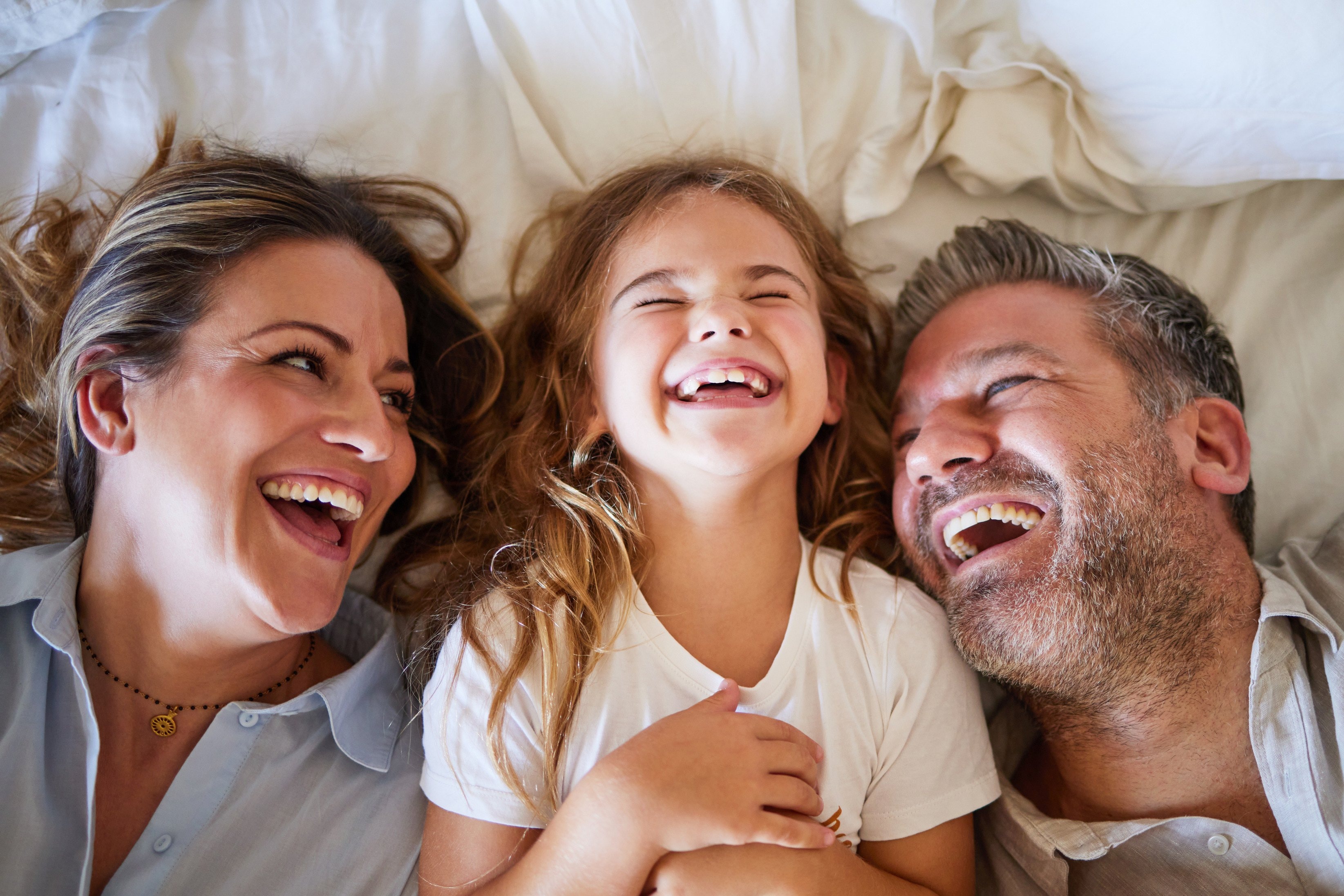 A mother, father and young daughter lying on a bed, laughing together