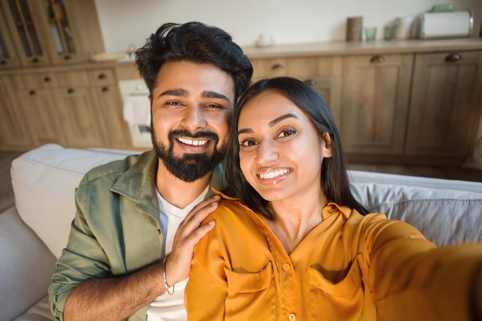 A smiling couple taking a selfie together on the sofa at home